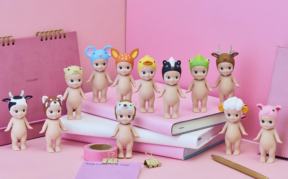 Sonny Angel style figurines in cute animal hats like deer, duck, cow, pig, arranged on pink books and desk with calendar, pen